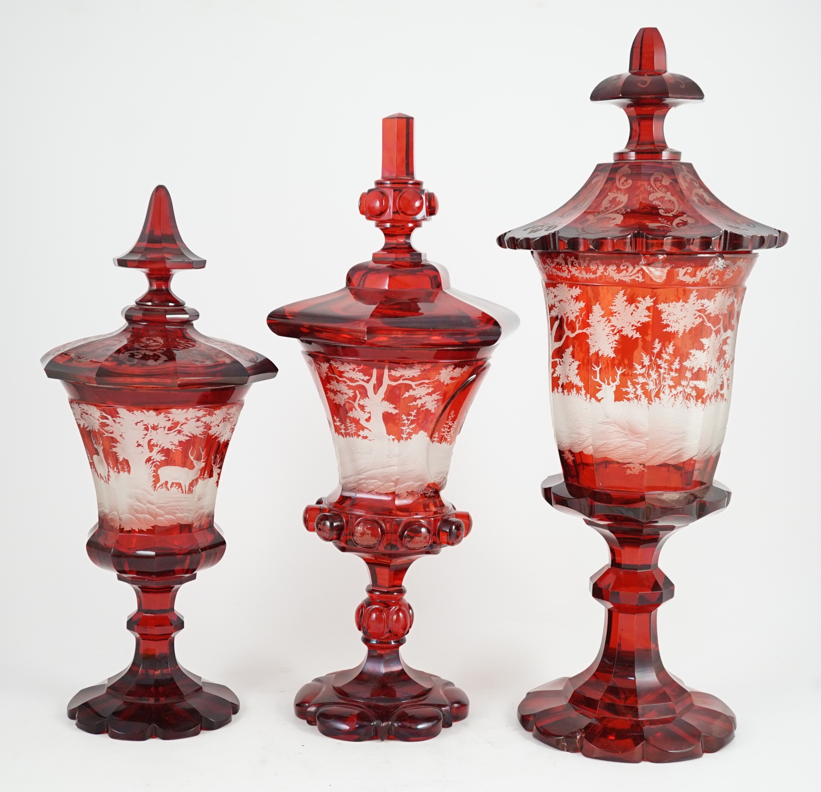 Three large Bohemian ruby stained glass goblets and covers, late 19th century, 38.5cm to 50.5cm high, rim chips